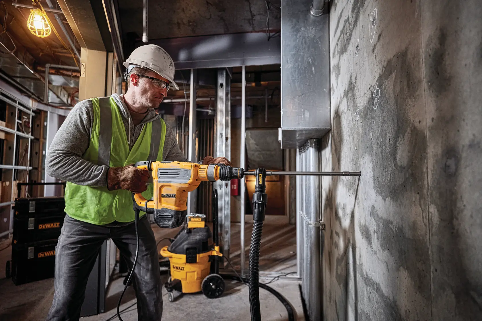 Kit DEWALT D25614K martillo combinado SDS+, mostrando un taladro de martillo amarillo y negro con mango lateral, posicionado frente a una caja plástica negra con el logotipo DEWALT. El kit incluye el martillo combinado, mango lateral y caja plástica.