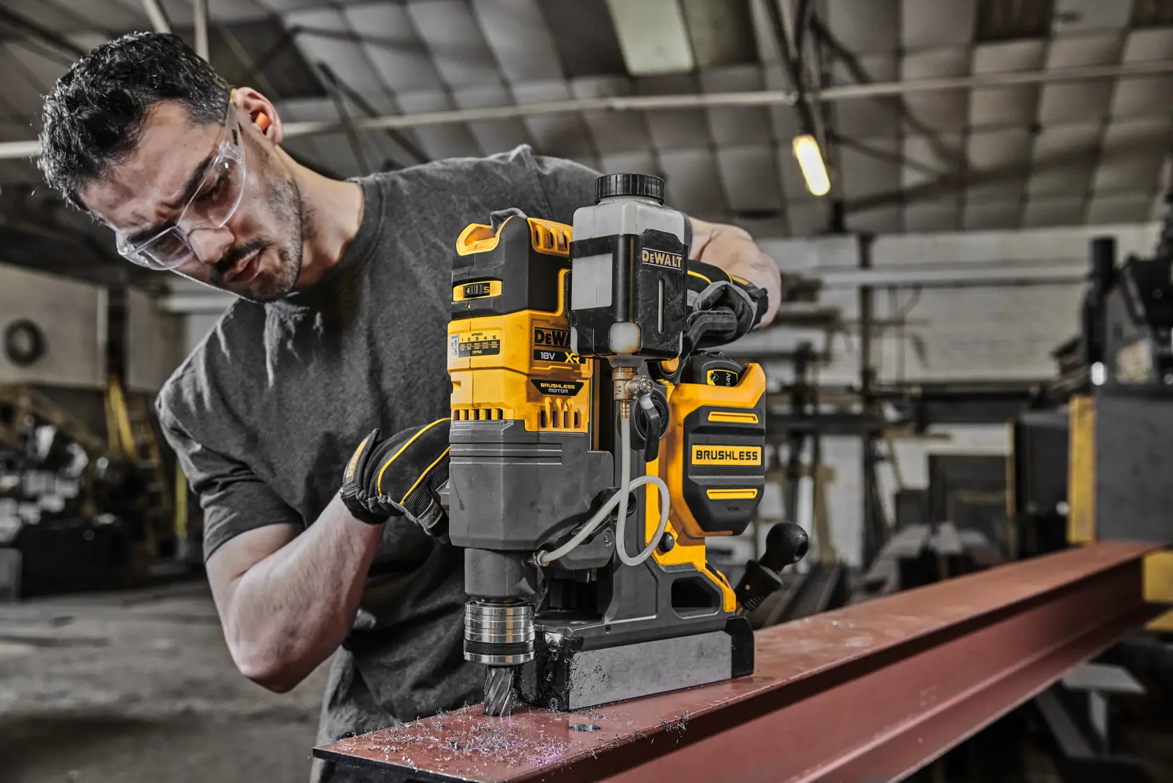 DEWALT magnetic drill in use on metal beam in workshop by a person with face obscured.