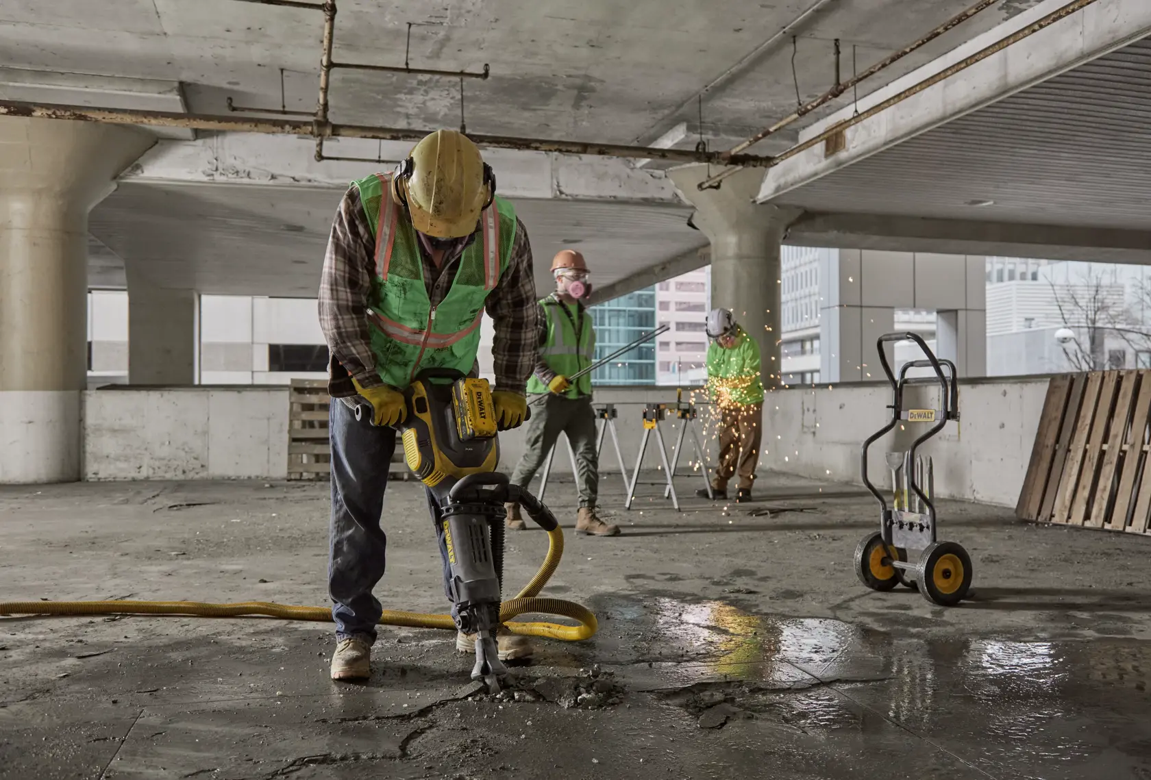 Workers use DEWALT tools for construction in a concrete building, including a jackhammer and equipment cart.