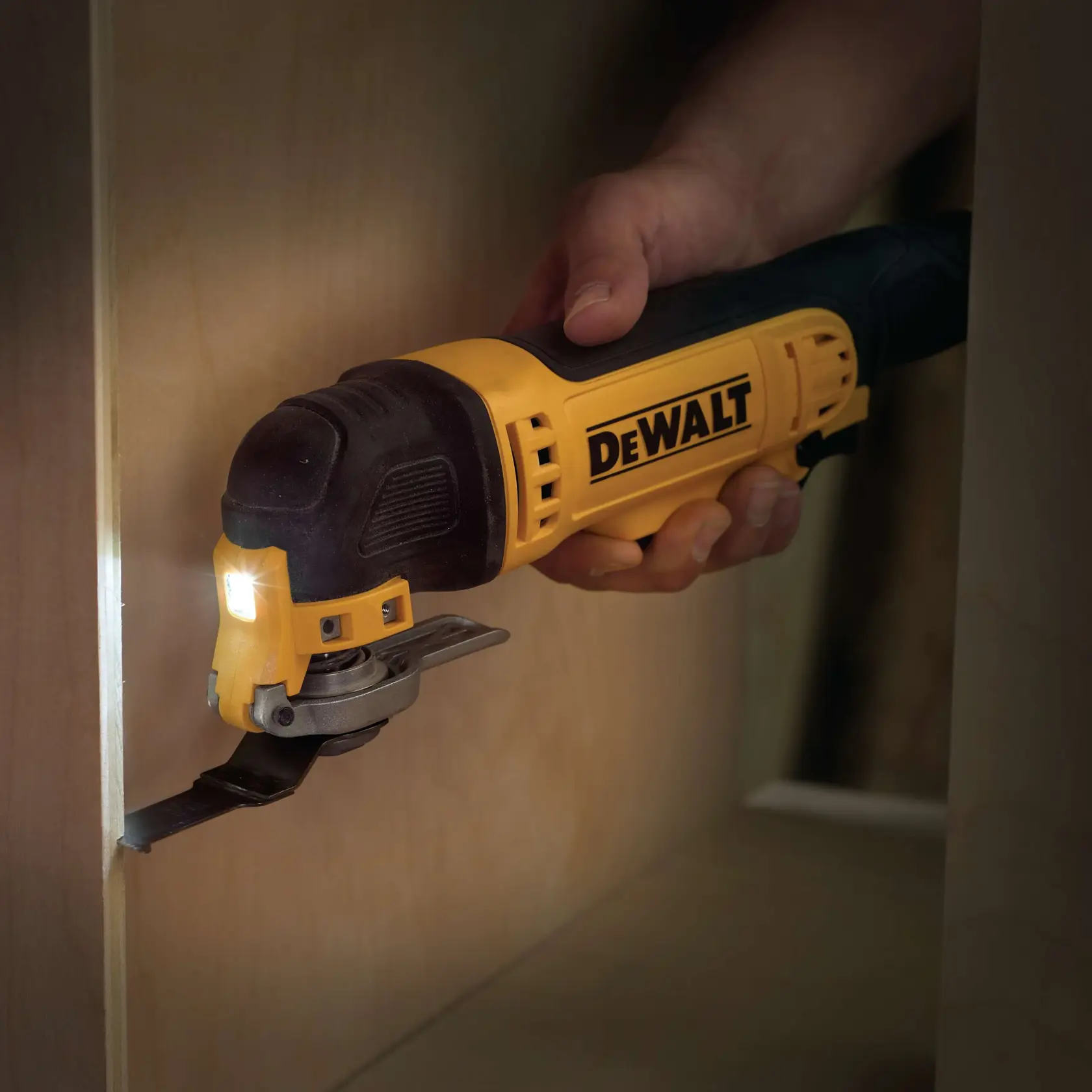 DEWALT oscillating multi-tool cutting wood with LED light, held by a hand close to a wooden surface.