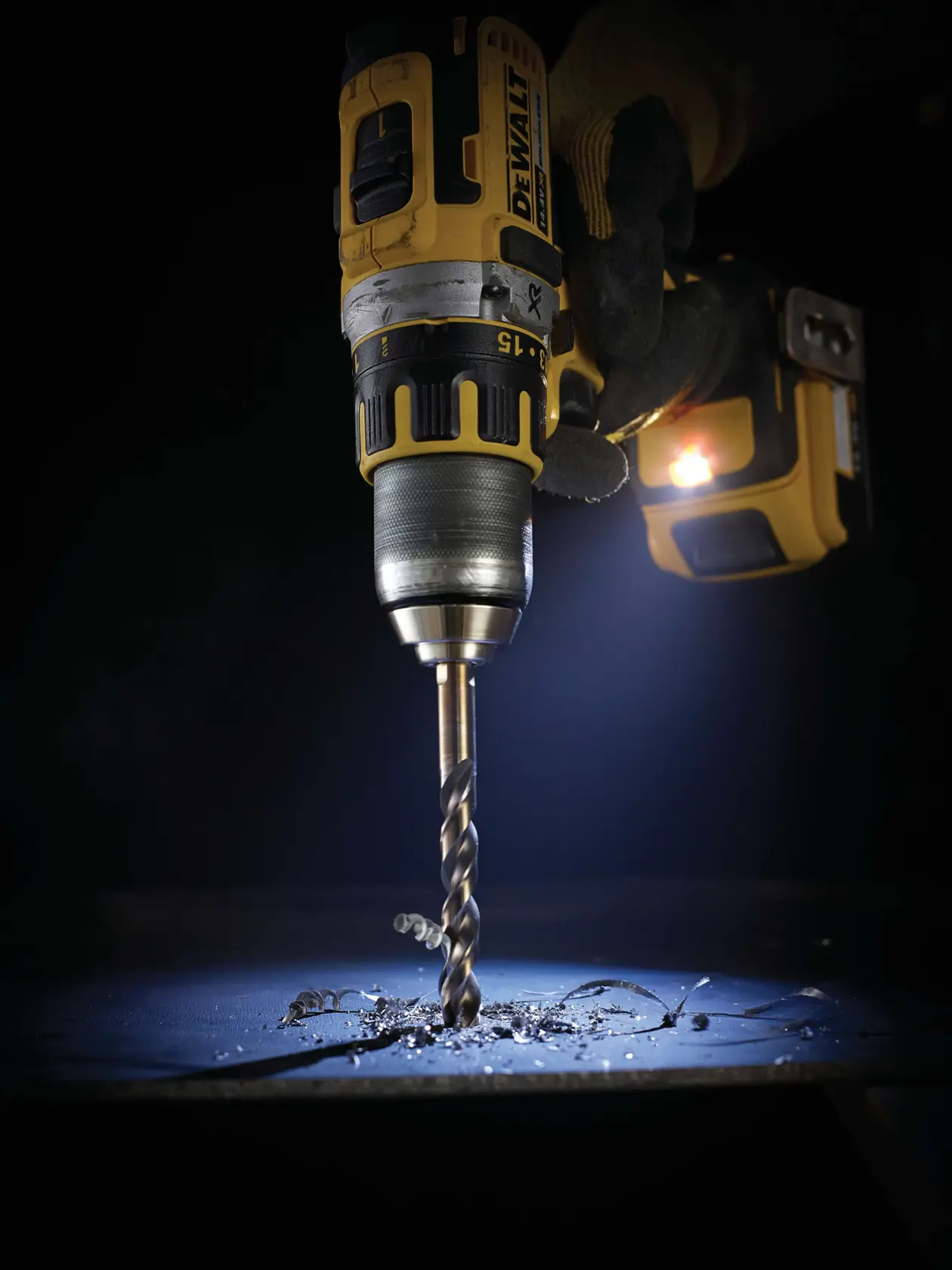 Taladro DEWALT perforando metal, virutas visibles y luz LED en un entorno oscuro.