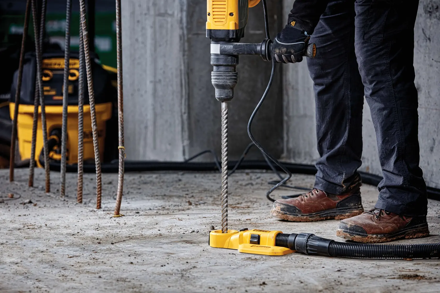 Persona usa taladro DEWALT con aspirador sobre piso de concreto en obra.