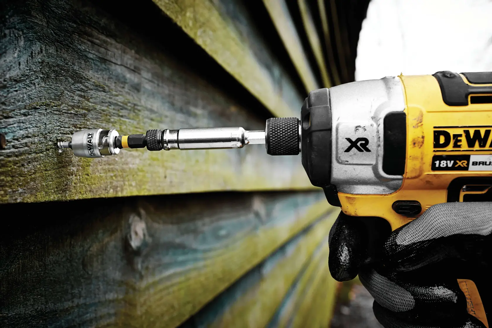 DEWALT power tool driving a screw into wood siding outdoors.