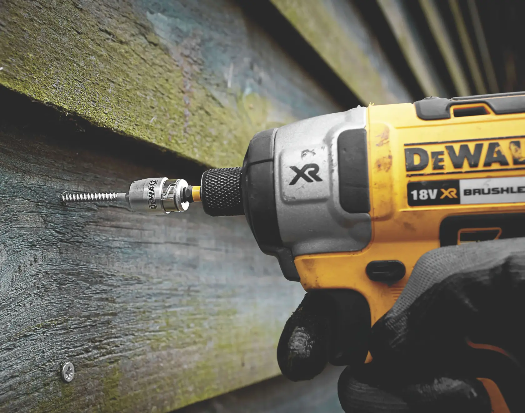 DEWALT cordless drill driving a screw into wood siding, close-up of tool and gloved hand.