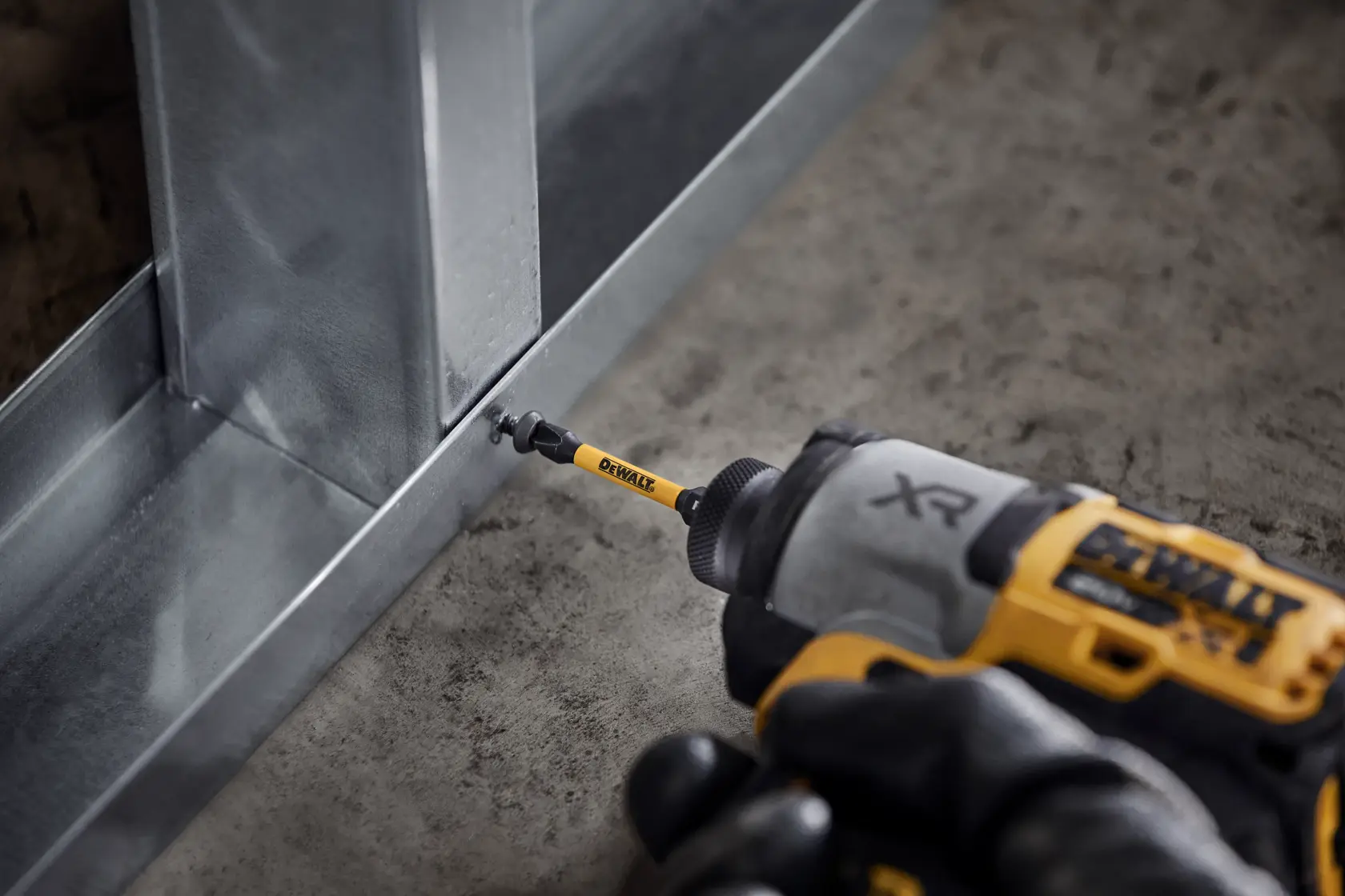 DEWALT impact driver with DT70536T bit driving a screw into a metal frame on a concrete floor.