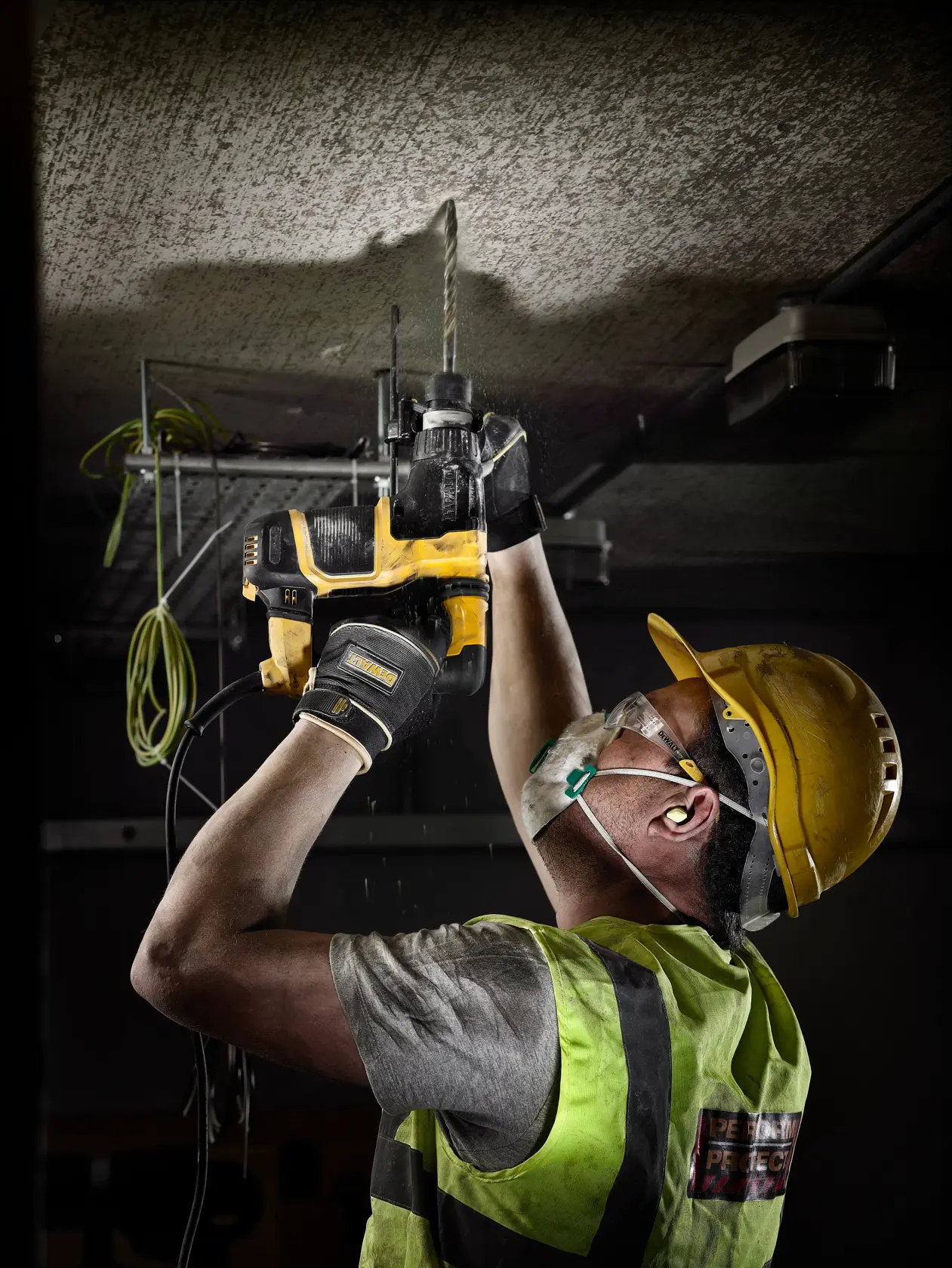Trabajador con equipo de seguridad utiliza un taladro DEWALT en el techo durante obra.