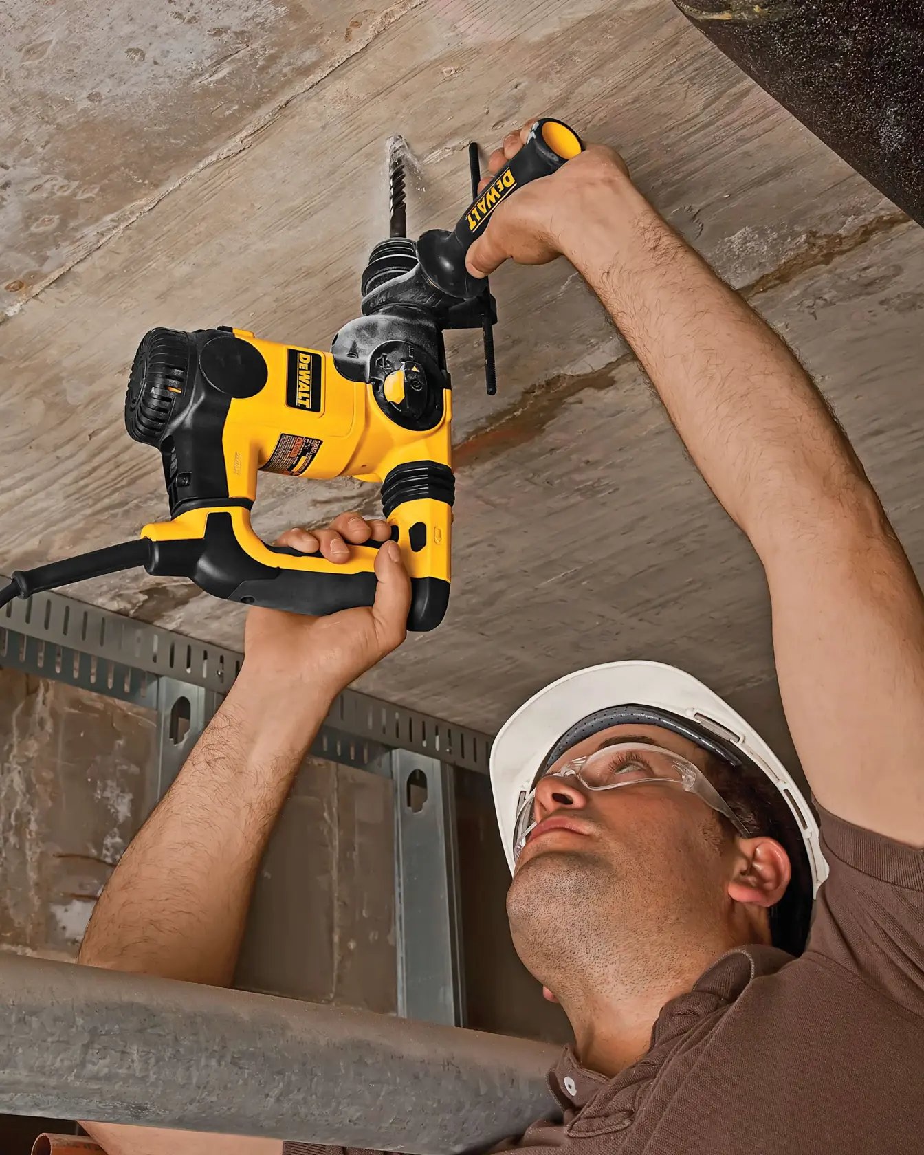 Persona usa taladro DEWALT amarillo en el techo, lleva casco de seguridad blanco.