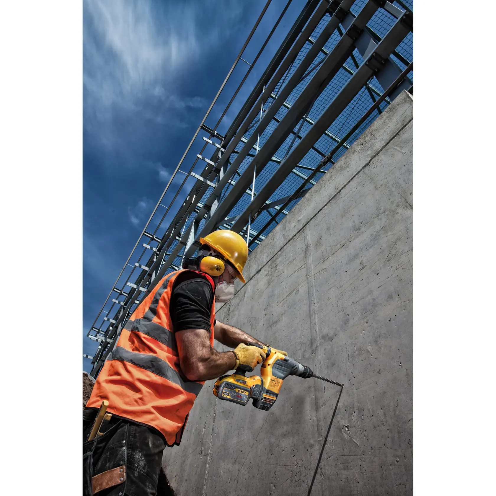 Operario con protección usa taladro Dewalt en pared de concreto en obra bajo cielo azul.