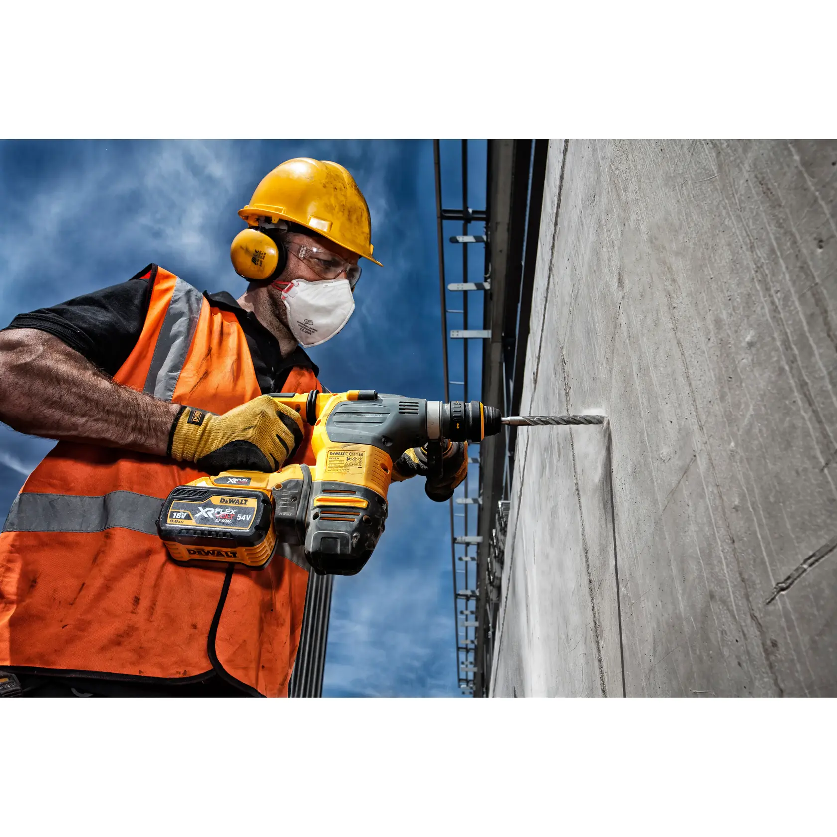 Trabajador perfora pared de hormigón con DEWALT DT9561, usando equipo de seguridad y chaleco naranja.