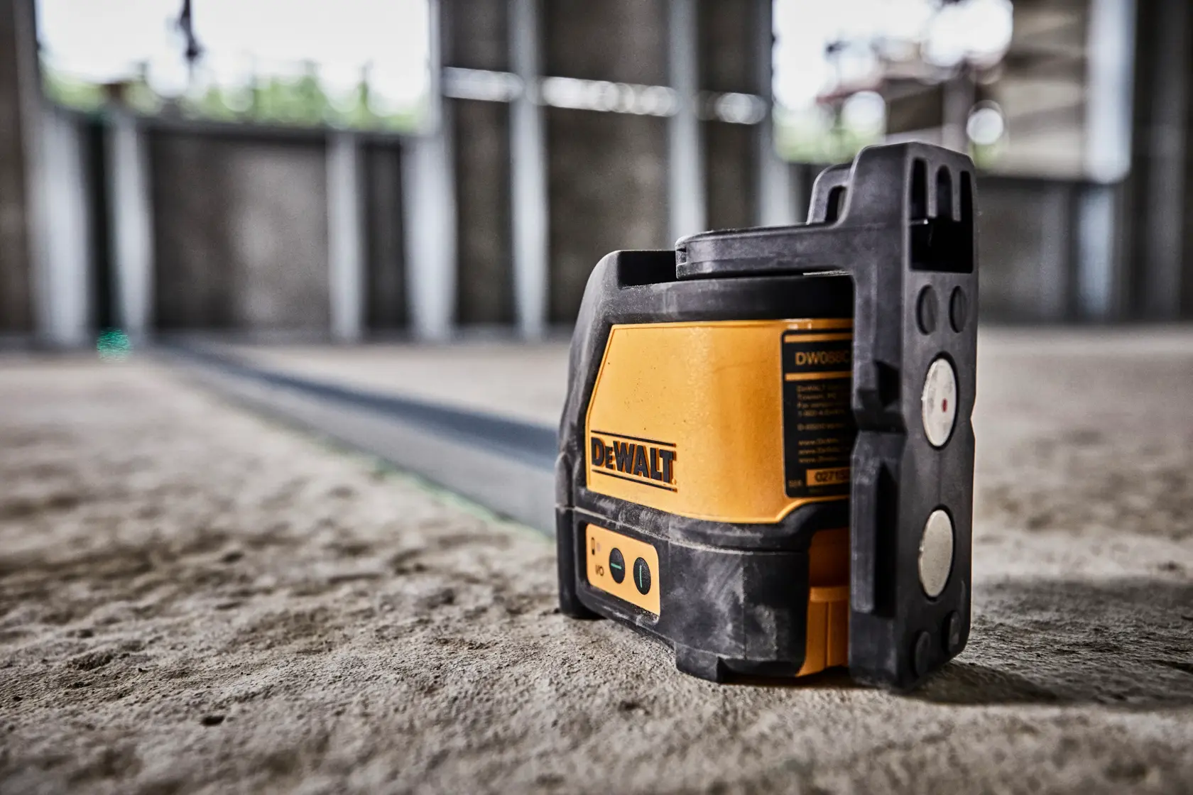 Un niveau laser à ligne verte DEWALT DW088CG placé sur un sol en béton dans un chantier, émettant une ligne laser verte pour