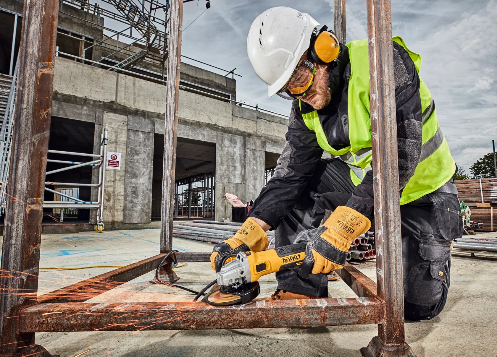 Trabajador usa amoladora DEWALT DWE4357 en marco metálico, lleva equipo de seguridad en obra.