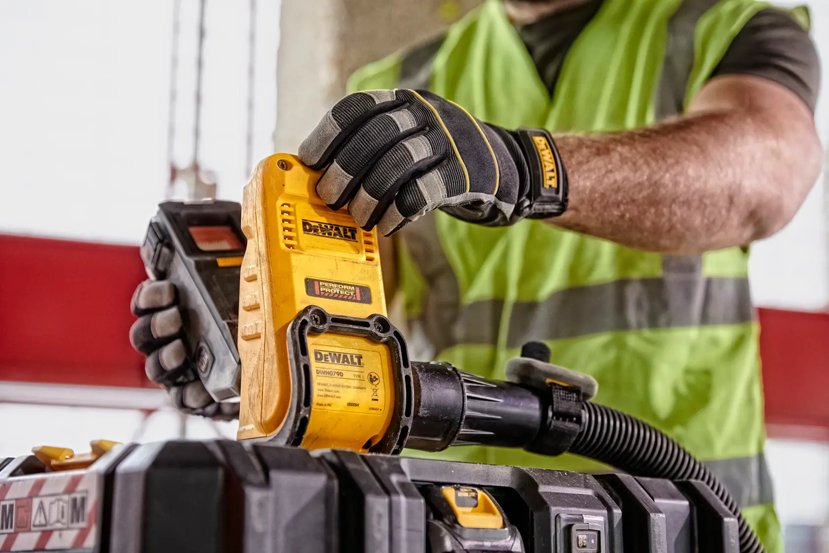 Person mit Handschuhen bedient DEWALT DWH079D Werkzeug neben Werkzeugkiste, Schlauch angeschlossen, Warnweste sichtbar.