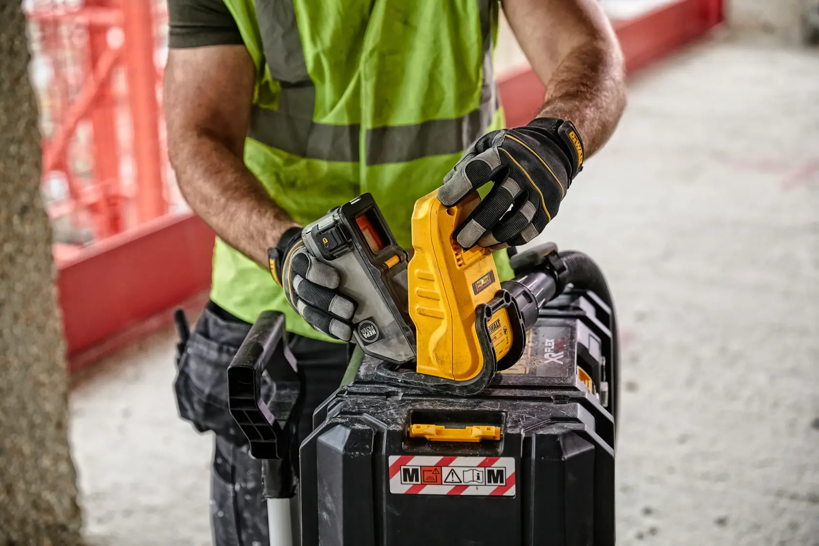 Arbeiter mit Handschuhen bedient ein DEWALT Werkzeug mit Akku auf einem Werkzeugkoffer.